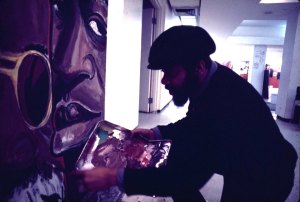 Mitchell Caton painting an unidentified indoor mural. Photo by Mark Rogovin, Public Art Workshop Mural Archive.